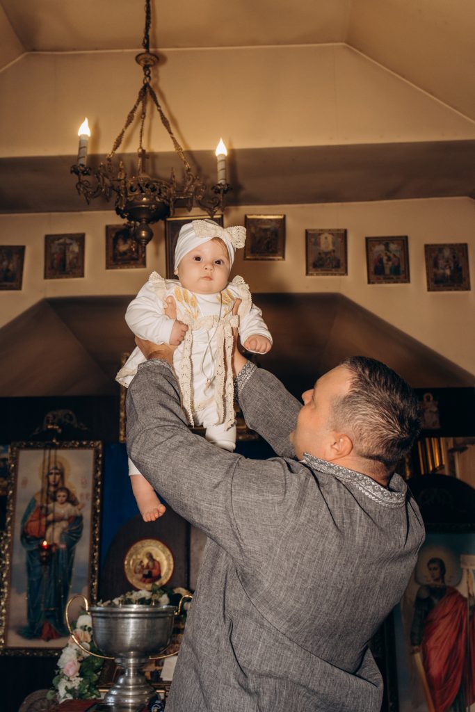 Чоловік піднімає Уляну вгору під церковною люстрою поруч із хрестильною купіллю