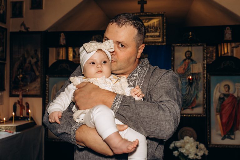 Чоловік у вишитій сорочці тримає Уляну на руках на тлі церковних ікон