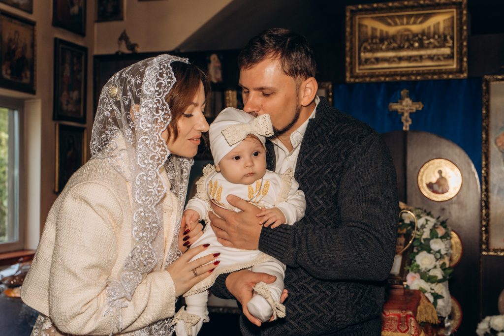 Жінка і чоловік тримають Уляну на руках у храмі, чоловік цілує дитину в голову