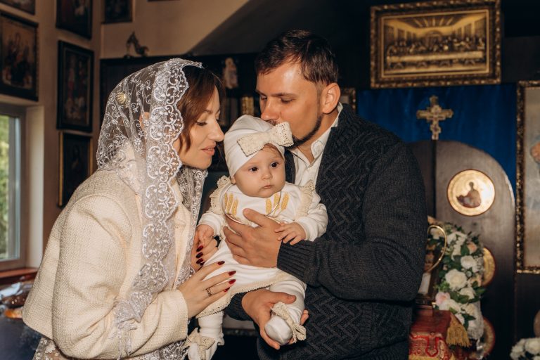 Жінка і чоловік тримають Уляну на руках у храмі, чоловік цілує дитину в голову