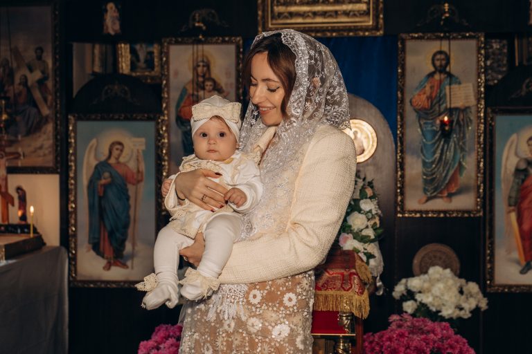 Жінка тримає Уляну на руках перед іконами у Церкві Всіх Святих ПЦУ