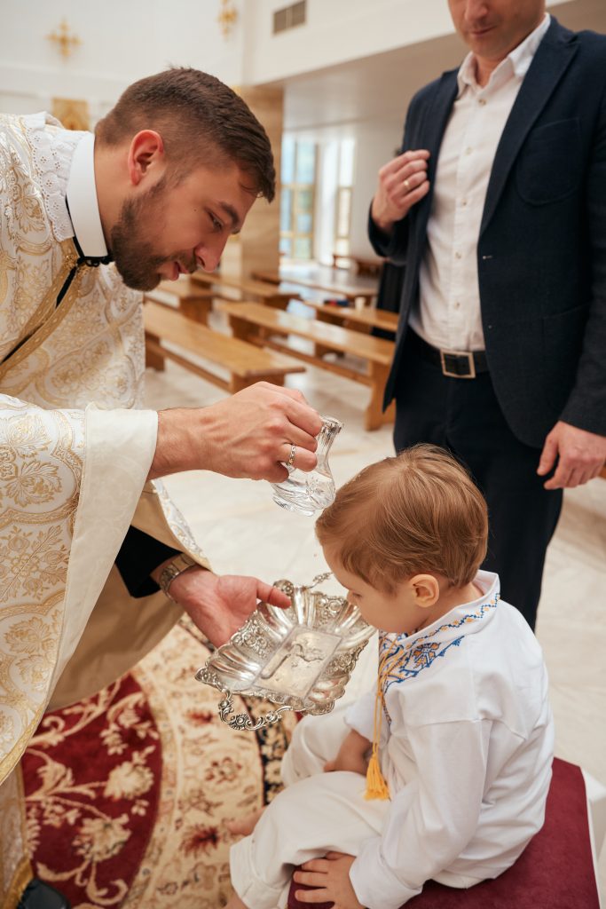 Священник здійснює обливання водою під час хрещення Ярослава, поруч стоїть дорослий чоловік