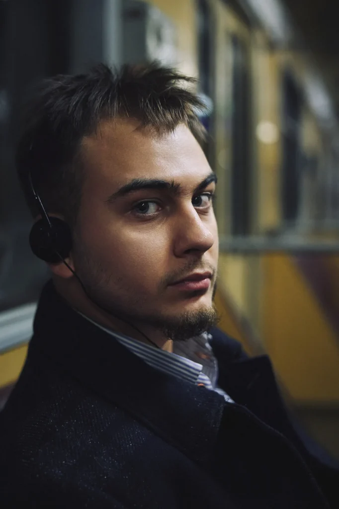 Кольоровий крупний портрет Арсена в навушниках, він дивиться в камеру через плече, вагон, Київ