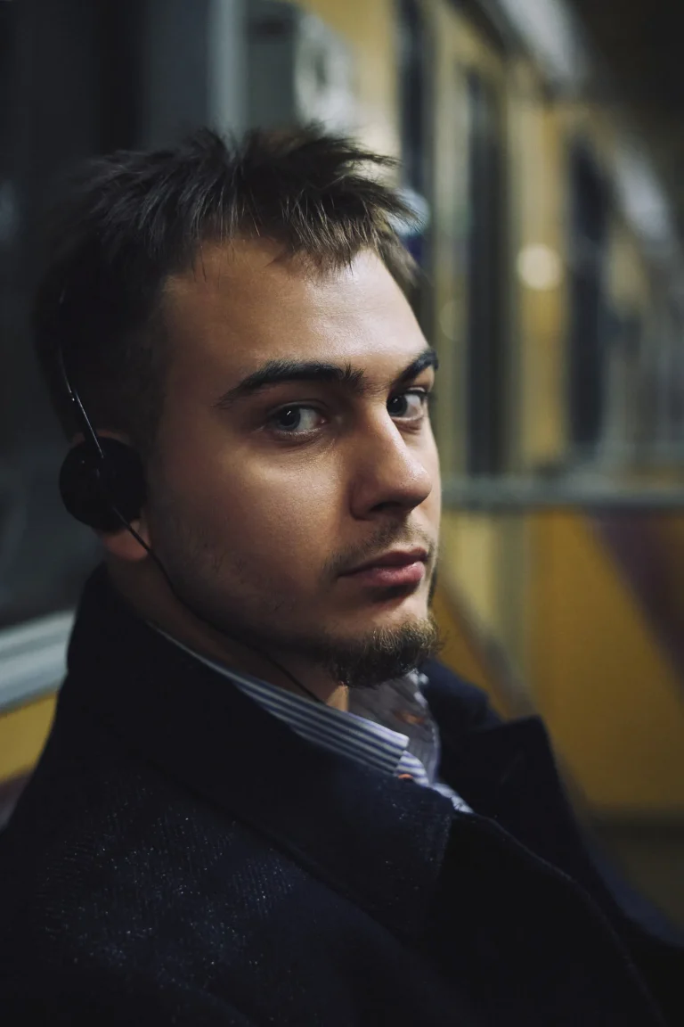 Кольоровий крупний портрет Арсена в навушниках, він дивиться в камеру через плече, вагон, Київ
