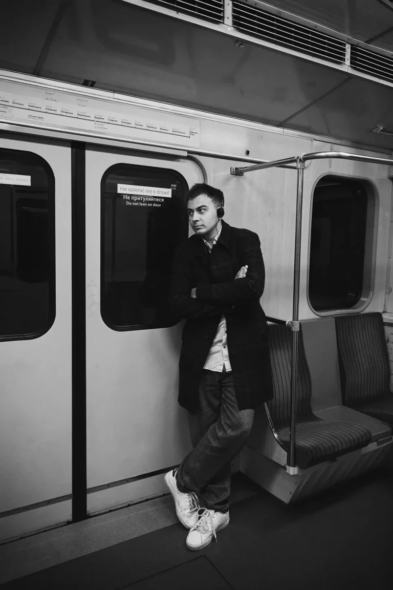 Чорно-біле фото: Арсен спирається на двері вагона метро, схрестивши руки й ноги, усміхається, Київ