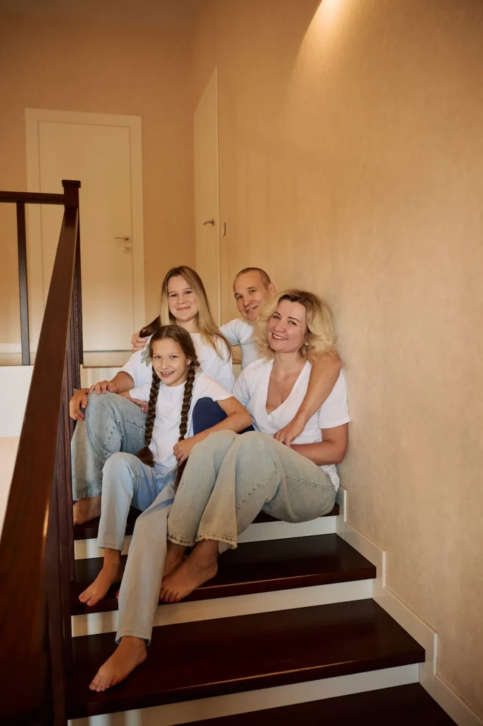 Родина з чотирьох сидить на дерев'яних сходах у будинку, усі в білому й джинсах, Київ