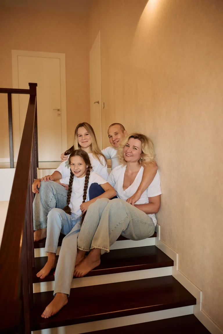 Родина з чотирьох сидить на дерев'яних сходах у будинку, усі в білому й джинсах, Київ