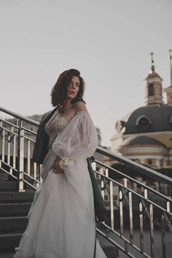 Анна з курткою на одному плечі стоїть на сходах, позаду храм із зеленим куполом, Київ