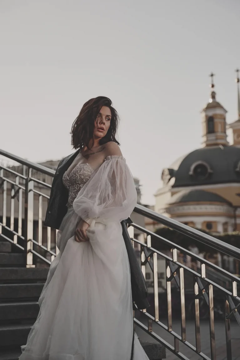 Анна з курткою на одному плечі стоїть на сходах, позаду храм із зеленим куполом, Київ